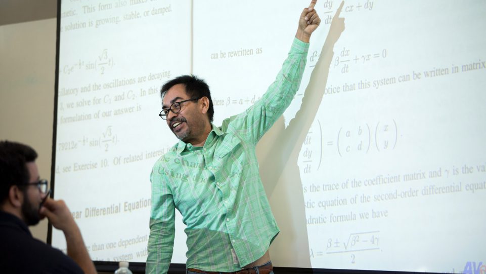 Male Instructor Lecturing in Front of a Black and White Projected Image of a Textbook