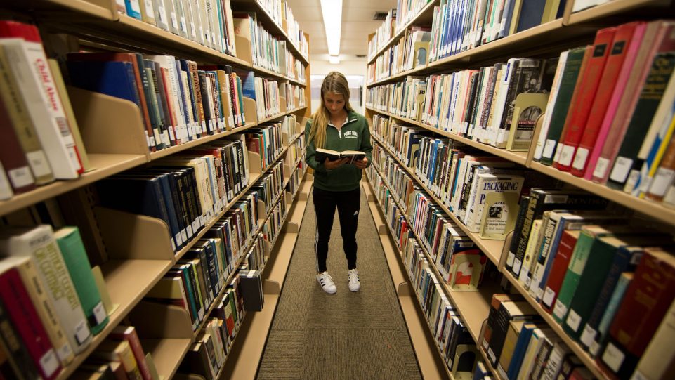 Female Student in the Library with Stacks of Books on the Left and Right