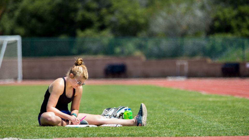 Female Student Stretching on the Grass Next to the Track