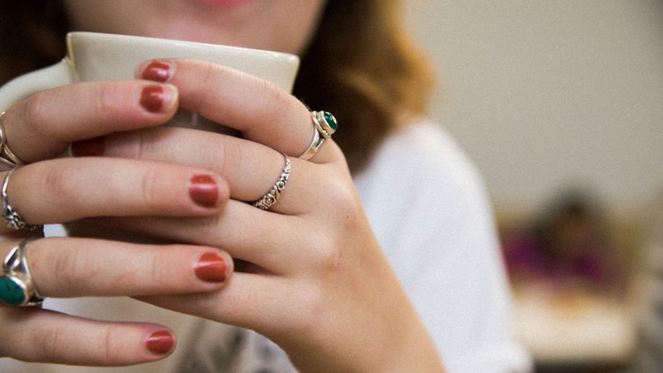 Close-Up Image of Female Subject's Hands Holding a Hot Beverage While She Speaks to Someone Off-Camera