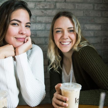 Two Seated Female Students Smile at Camera While One Enjoys a Cafe Beverage Join Today Welcome to Sites.Dot